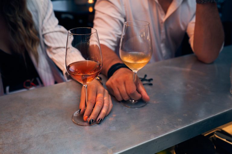 man and woman holding glasses of wine next to each other at the bar